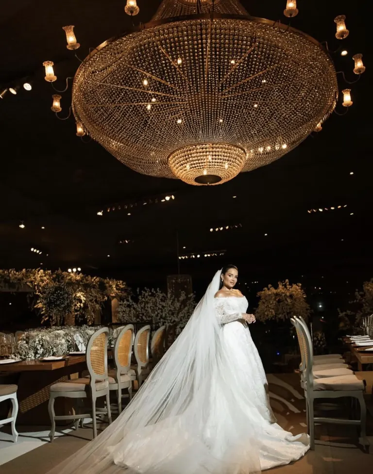 Noiva com véu longo em salão iluminado por lustre de cristal