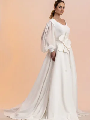 Vestido de noiva Danielle: evasê liso, mangas longas transparentes e flor escultural na cintura. Coleção Ateliê Guinza