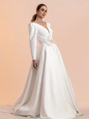 Vestido de noiva Elegance: decote em V, mangas longas estruturadas e flor na cintura. Coleção Ateliê Guinza