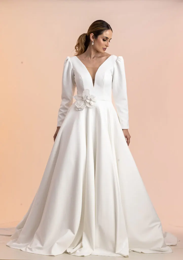 Vestido de noiva evasê com decote em V, mangas longas e flor na cintura