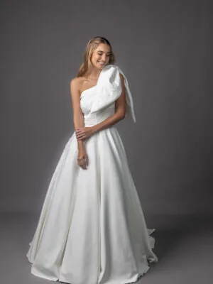 Vestido de noiva Joan: um ombro só com laço escultural e saia ampla lisa. Coleção Ateliê Guinza