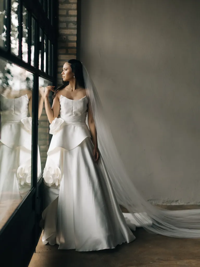 Noiva com vestido de laço escultural junto à janela